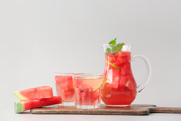Jug and glasses of cold watermelon lemonade on light background