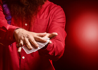 Male magician with cards on dark background