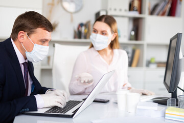 Director and secretary in protective medical masks work in the office
