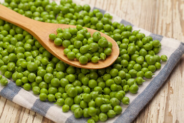 Organic fresh green peas in wooden spoon on vintage wooden background