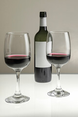 Vertical shot. Two glasses and a bottle of red wine on a blurred homogeneous background. 