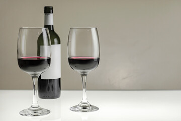 Two glasses and a bottle of red wine on a light table.