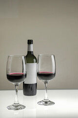 Vertical shot. Two glasses and a bottle of red wine on a blurred homogeneous background. 