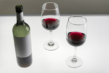 Two glasses and a bottle of red wine on a light background. Horizontal photo
