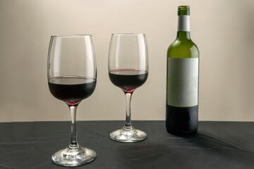 Two glasses and a bottle of red wine on a light table.