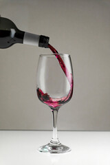 Red wine is poured from a bottle into a glass on a blurred background, close-up. Vertical photo