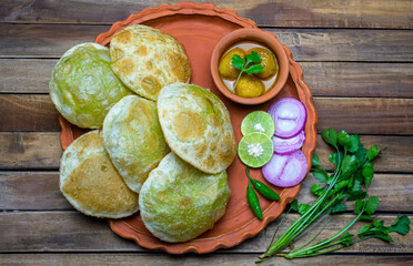 Traditional Bengali cuisine - Green peas kachori or Koraishutir kochuri in a earthenware plate along with a bowl of Spicy dum aloo curry, onion, lemon and green salad.