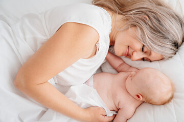 mom is mom is lying down with a baby in a white bed after feeding breast milk. 
