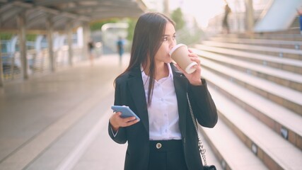 A young business woman wearing black suit is using smart phone , holding a cup of coffee in the city, Business Lifestyle Concept