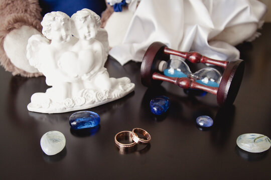 Groom's morning. Wedding accessories in blue colors. Tie-wedding rings, angels statuettes and hourglass on black background. Two wedding rings on a dark wood background 
