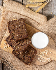 Rye bread with sunflower seeds on a serving board. Pieces of bread on a board with a glass of milk on a wooden rustic table. Healthy rye bread	