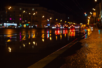 selective focus of city road and car with out of focus lights. Water and rain on the asphalt and abstract image of lanterns in the night city
