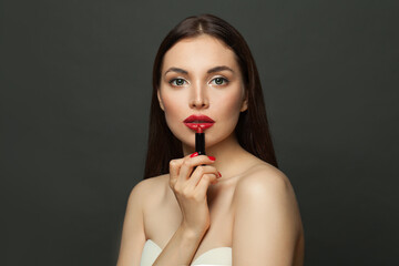 Beautiful young woman holding red lipstick near lips on black background