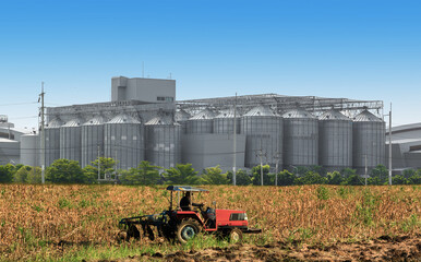 Agricultural Silos - Building Exterior, Storage and drying of grains, wheat, corn, soy, sunflower against the blue sky  with farm tractors in the foreground.