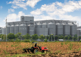Agricultural Silos - Building Exterior, Storage and drying of grains, wheat, corn, soy, sunflower against the blue sky  with farm tractors in the foreground.