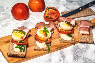 crispbreads with smoked ham, tomatoes and eggs on a cutting board