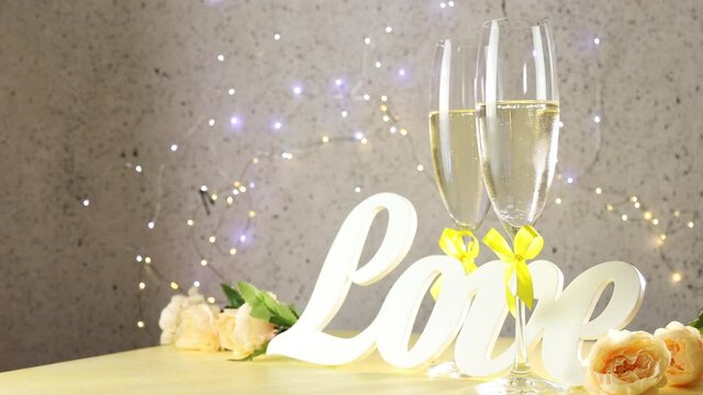 Two champagne glasses with yellow bows standing on table with love letters and roses rolled of circles, bokeh lights, St. Valentine or wedding greeting card