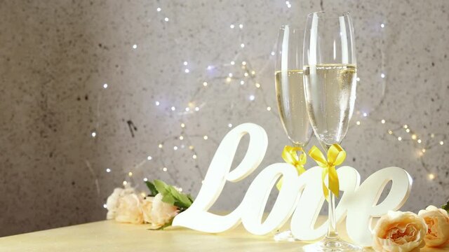 Two champagne glasses with yellow bows standing on table with love letters and roses rolled of circles, bokeh lights, St. Valentine or wedding greeting card