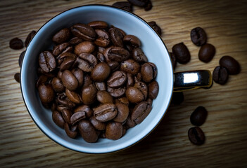 Top down photo of fresh coffee beans in an espresso cup surrounded by coffee beans on a kitchen work 
