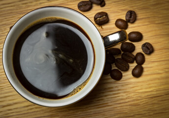 Top down photo of freshly poured coffee in an espresso cup surrounded by coffee beans on a kitchen work surface