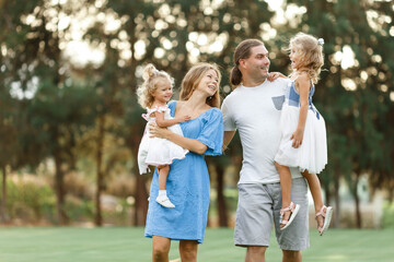 Naklejka premium Parents hold daughters in their arms In Countryside, enjoing time together. Happy family concept. Blurred trees background.