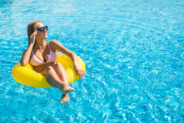 Happy young woman in bikini float with yellow rubber inflatable ring, playing and having a good time at water fun park pool, on a summer hot day