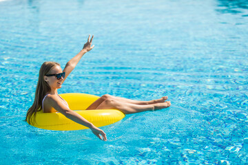 Summer vacation. Beautiful slim young woman enjoying an aqua park floating in a yellow big ring on sparkling blue pool