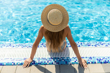 Rear view of beautiful young woman in bikini sitting by swimming pool