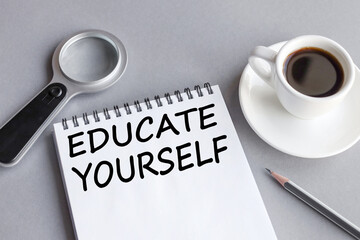 educate yourself, text on white notepad paper on gray background. magnifier. a cup of coffee