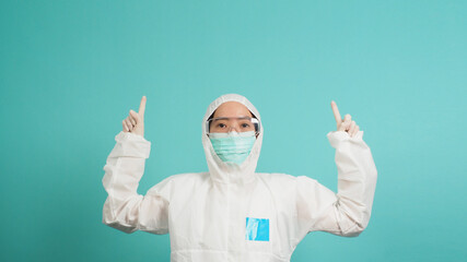 Asian woman in PPE suit  wear face mask is pointing finger up on green or Tiffany Blue background.