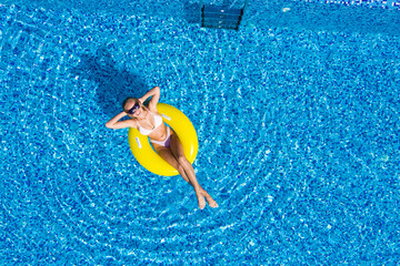 Aerial view of young woman swimming on the inflatable big yellow ring in pool