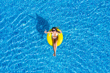 Aerial view of young brunette woman swimming on the inflatable big donut in the transparent turquoise sea. Top view of slim lady relaxing on her holidays