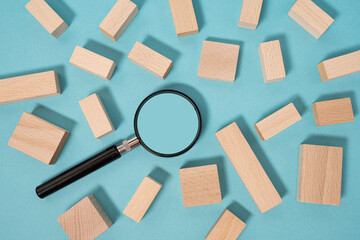 Search concept, recruitment. Magnifying glass and wooden blocks on blue background