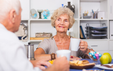 Happy senior woman drinking tea and chatting with his old friend at home