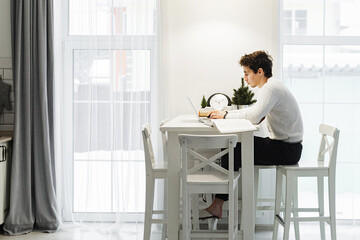 A man working on a laptop at home at bright kitchen