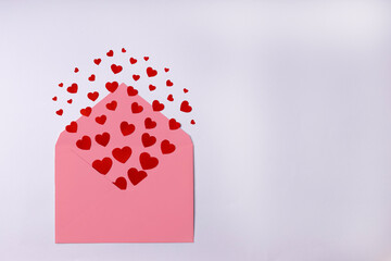 Pink envelope with red small paper hearts on the right side on white background. Valentine's Day, February 14, love concept. Flat lay, top view, copy space.