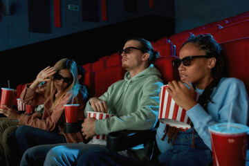 A group of young friends wearing glasses, looking emotional while watching movie together in cinema auditorium