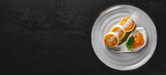 cheese pancakes with sour cream and strawberry sauce on plate on Dark grey black slate background