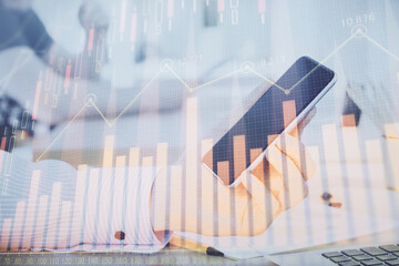 Double exposure of man's hands holding and using a digital device and forex graph drawing. Financial market concept.