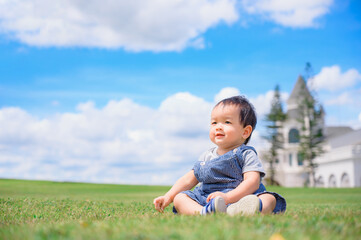 Naklejka na ściany i meble Boy among green grass s on a summer day. A small child has fun in the fresh air. Baby explores the nature with blue sky