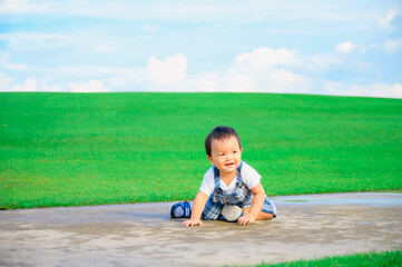 Fototapeta na wymiar Boy among green grass s on a summer day. A small child has fun in the fresh air. Baby explores the nature with blue sky