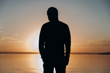 a man looks at the lake against the background of the sunset