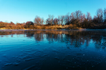 Fototapeta premium Winter landscape with frozen river and coastline on a sunny day. Copy space. Selective focus