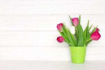 Tulip flower bouquet in bucket on wood table near white painted wooden board wall. Copy space. Spring rustic background
