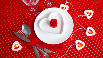 A white plate with a knife and fork on a bright red background. Heart shaped white plate. Valentines Day. The view from the top.