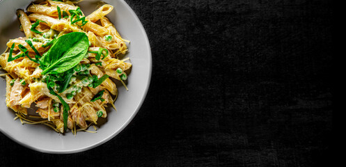 Penne pasta with chicken meat, cream sauce and cheese in a bowl on Dark grey black slate background