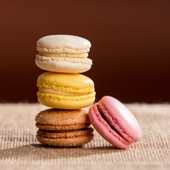 Close-up on four French macarons, 3 on top of each other forming a small column and a 4th one slanted on the side, placed on burlap with a chocolate background