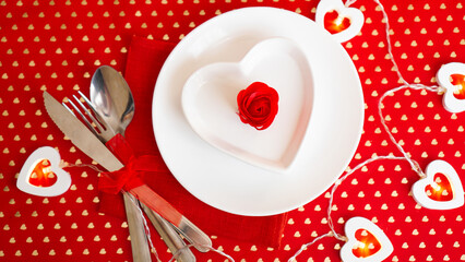 A white plate with a knife and fork on a bright red background. Heart shaped white plate. Valentines Day. The view from the top.