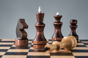 Wooden chess pieces on a chessboard, the white king lies in front of the black pieces, the concept...