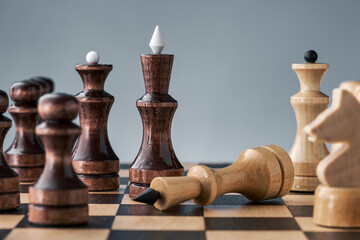 Wooden chess pieces on a chessboard, the white king lies in front of the black pieces, the concept of strategy, planning and decision making. The concept of leadership and teamwork to achieve success.